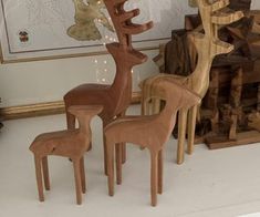 three wooden deer sculptures sitting on top of a white floor next to a pile of logs