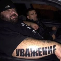 two men sitting in the back seat of a car with their arm tattoos on them