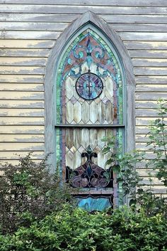 an old stained glass window in the side of a building with shrubbery around it