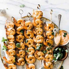 shrimp skewers on a platter with dipping sauce and garnished greens