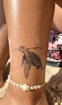 a woman's foot with a turtle tattoo on the side and pearls around her ankles