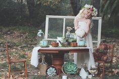 a woman standing in front of a table filled with potted plants and other items