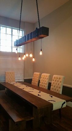 a dining room table and chairs with lights hanging from the ceiling above it, in front of a window