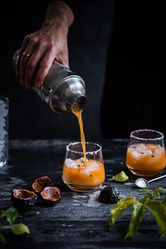 a person pouring orange juice into two glasses on a table next to some other drinks