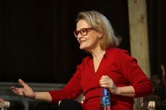 an older woman sitting in a chair with her hands out to the side and talking