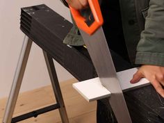 a person holding a large pair of scissors on top of a piece of wood next to a step ladder