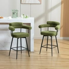 two green upholstered barstools sit in front of a white counter