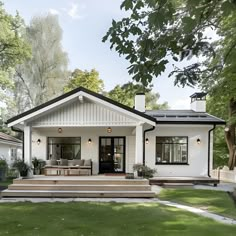 This charming Scandinavian bungalow features a classic white exterior with black trim and a gabled roof. The inviting front porch, complete with cozy seating and potted plants, enhances its appeal. Large windows flood the interior with natural light, creating a bright and welcoming atmosphere. The well-manicured yard and minimalistic design reflect traditional Scandinavian architecture, offering a serene and stylish retreat. White Traditional House Exterior, Bungalow With Front Porch, Updated Bungalow Exterior, Gabled Porch Roof, Gable Roof House Design, White Bungalow House, Front Porch On A Ranch Style Home, Gable Back Porch, Bungalow Farmhouse Exterior