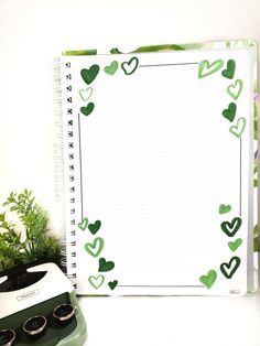 a notebook with green hearts on it next to an old typewriter and potted plant