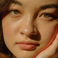 a close up of a woman's face with her hand on her cheek and one eye open