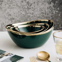 three green bowls with gold rims on a white table next to a glass of water