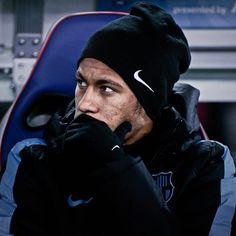 a man wearing a black hat and holding his hand to his face while sitting on a bench