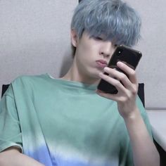 a young man with blue hair is looking at his cell phone while sitting in a chair