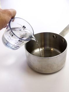 a person pouring water into a pan with a measuring cup