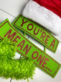 two green christmas signs sitting on top of a white tile floor next to a santa hat