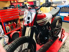 a red and white motorcycle parked on top of a metal platform in a room filled with tools