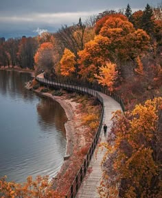 a person walking down a path next to a body of water in the fall season