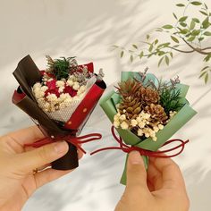 two hands holding small bouquets with pine cones and flowers