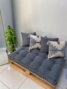 a couch made out of wooden pallets with pillows on the top and bottom, in front of a potted plant