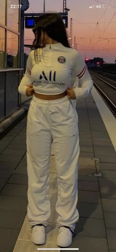 a woman in white is standing on the train platform with her hands behind her back