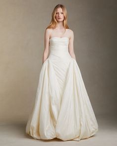 a woman in a white wedding dress standing on a gray background with her hands behind her back