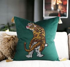 a green pillow with a tiger on it sitting on a couch next to a white chair