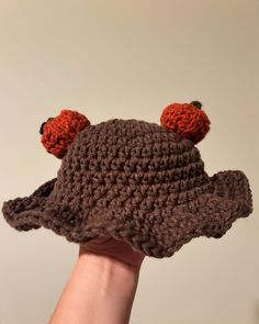 a hand holding up a crocheted hat with ears and two orange balls on it