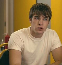 a young man sitting at a table with a remote in his hand and looking off to the side