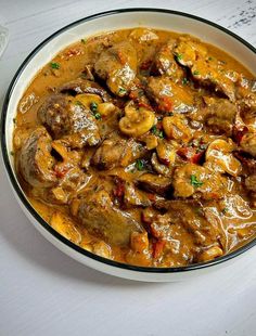 a white bowl filled with meat and mushrooms covered in gravy on top of a table