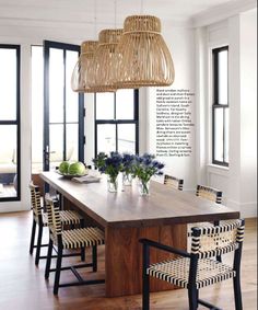 a dining room table with chairs and flowers in vases on the centerpiece, next to large windows