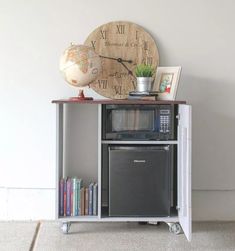 an old fashioned microwave is on top of a small cabinet with a clock above it