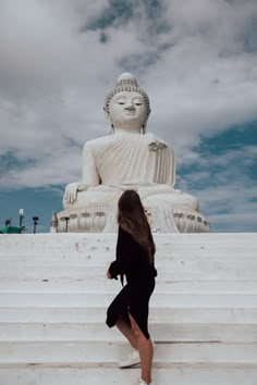 a woman is walking up some steps towards a large buddha statue