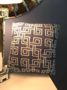 a blue and white crocheted pillow sitting on top of a table next to a mirror