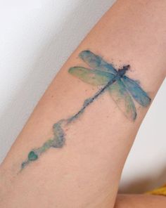 a blue and green dragonfly tattoo on the right arm with watercolor paint splatters