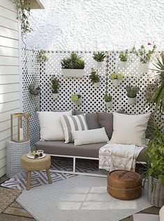 an outdoor seating area with potted plants on the wall and pillows on the floor