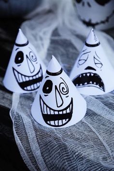 three paper hats with faces painted on them sitting on a cloth covered surface, one is white and the other is black