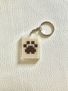 a cross stitch keychain is shown on a white leather surface with a black and brown design