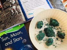 an open book on the moon and stars next to a plate with green stuff in it