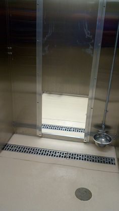 a stainless steel shower stall with the door open and floor drain in front of it