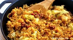 a skillet filled with stuffing and vegetables on top of a table next to a wooden spoon