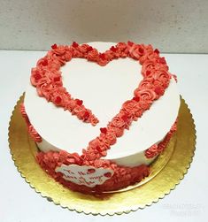 a heart shaped cake on a gold plate with red frosting and roses in the shape of a heart