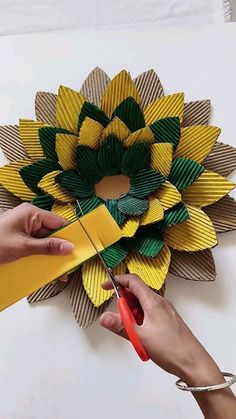 someone cutting paper with scissors on top of a yellow and green sunflower flower ornament