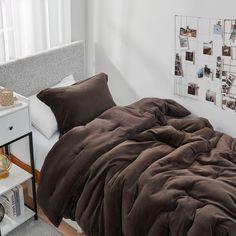 a bed with brown comforter and pillows in a white room next to a window