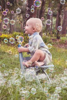 a toddler sitting on a chair with soap bubbles in the air and trees in the background