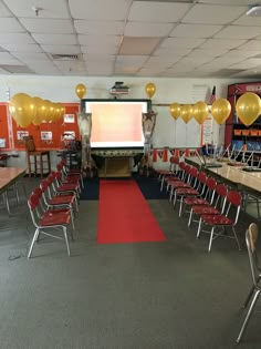 an empty classroom with red chairs and yellow balloons on the ceiling, in front of a projector screen