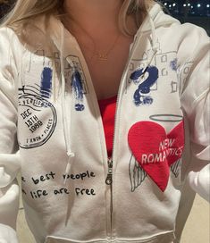 a woman wearing a white hoodie with red heart patches and writing on the side