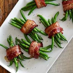 green beans and bacon wrapped in bacon on a white platter with a wooden table