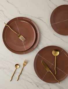 three brown plates with gold forks and spoons on white marble countertop next to each other