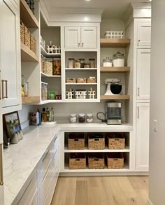 a kitchen with white cabinets and lots of baskets on the counter top in front of it