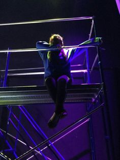 a woman sitting on top of a metal platform in front of a purple and blue light